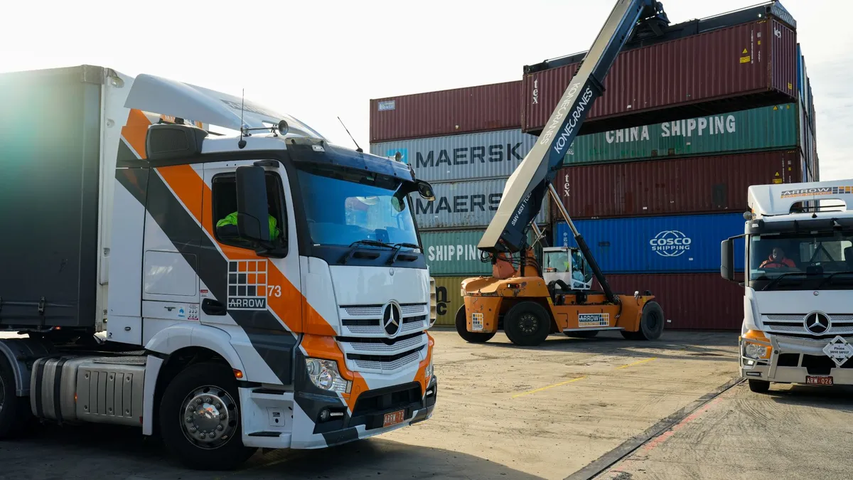 An Arrow Transport prime mover and a reach stacker moving containers in a wharf cartage yard at first light.